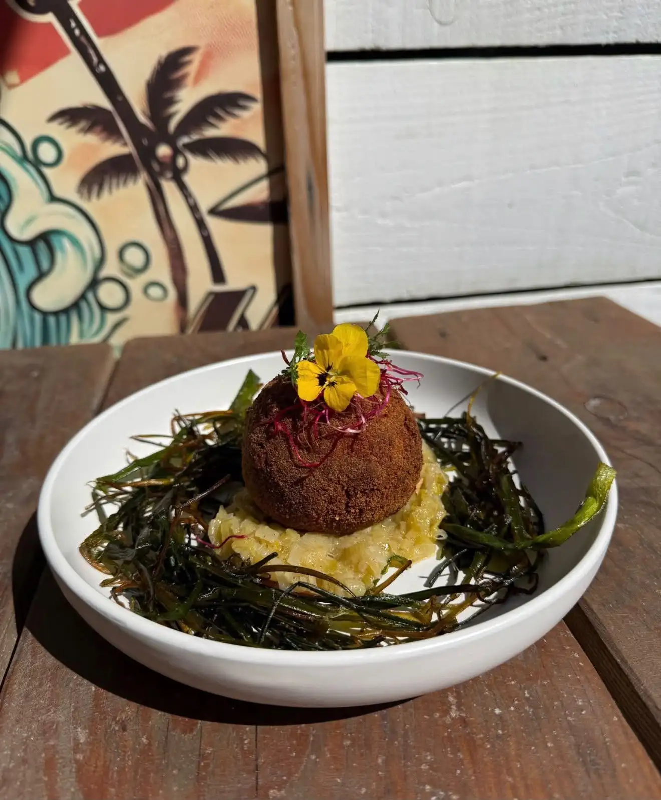 Croquette croustillante posée sur un lit de salicornes, avec une fleur comestible